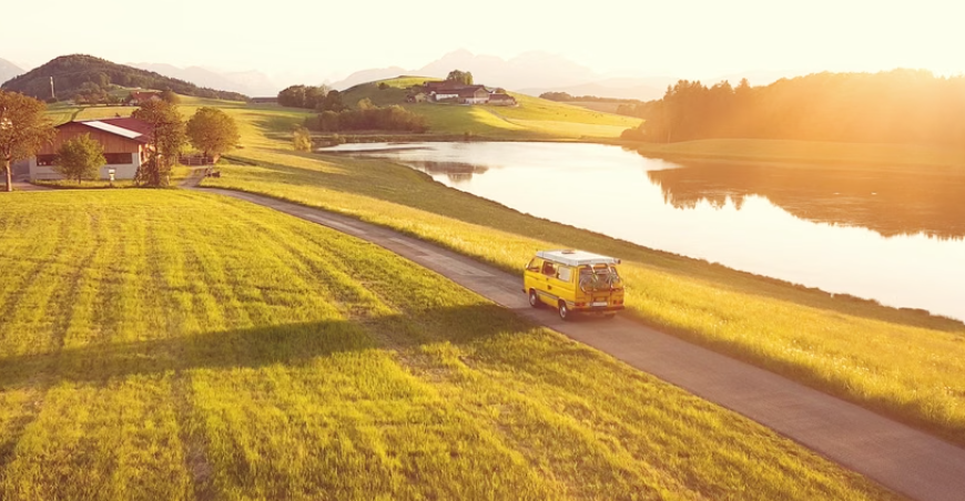 Gelber Campervan fährt durch eine ländliche Seenlandschaft.