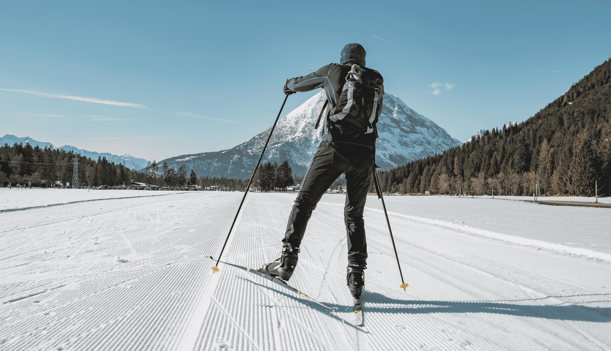Person beim Langlaufen vor einer verschneiten Bergkulisse.