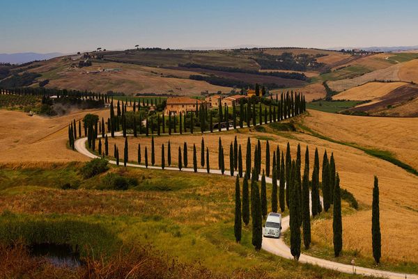 Wohnmobil auf kurviger Straße durch typische Zypressenlandschaft in Italien