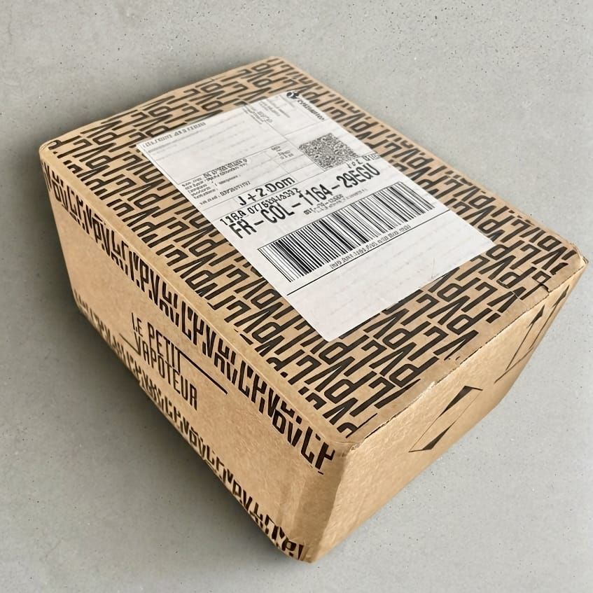 Colis Lucky Bag du Petit Vapoteur fermé, avec étiquette d'expédition, posé sur un fond gris.