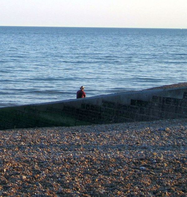Man in hat sitting on Brighton Beach watching the waves
