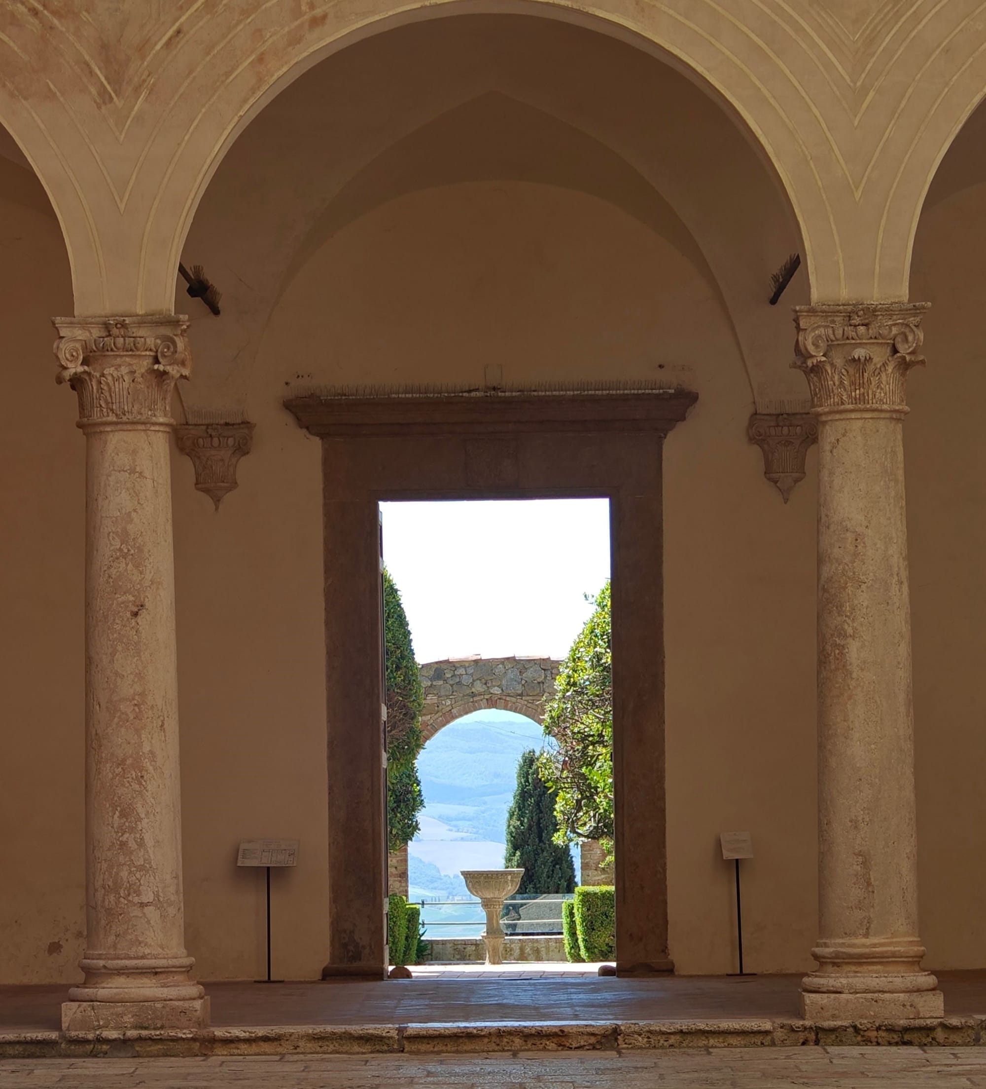 A sequence of stone arches and doorways opening onto a sunlit garden and distant landscape.