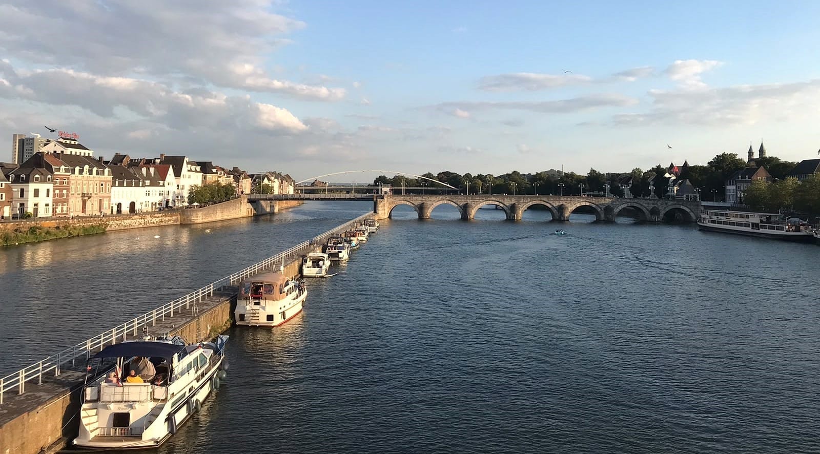 Evening view across the River Maas towards the Sint Servaasbrug in Maastricht, with boats moored along the quay.