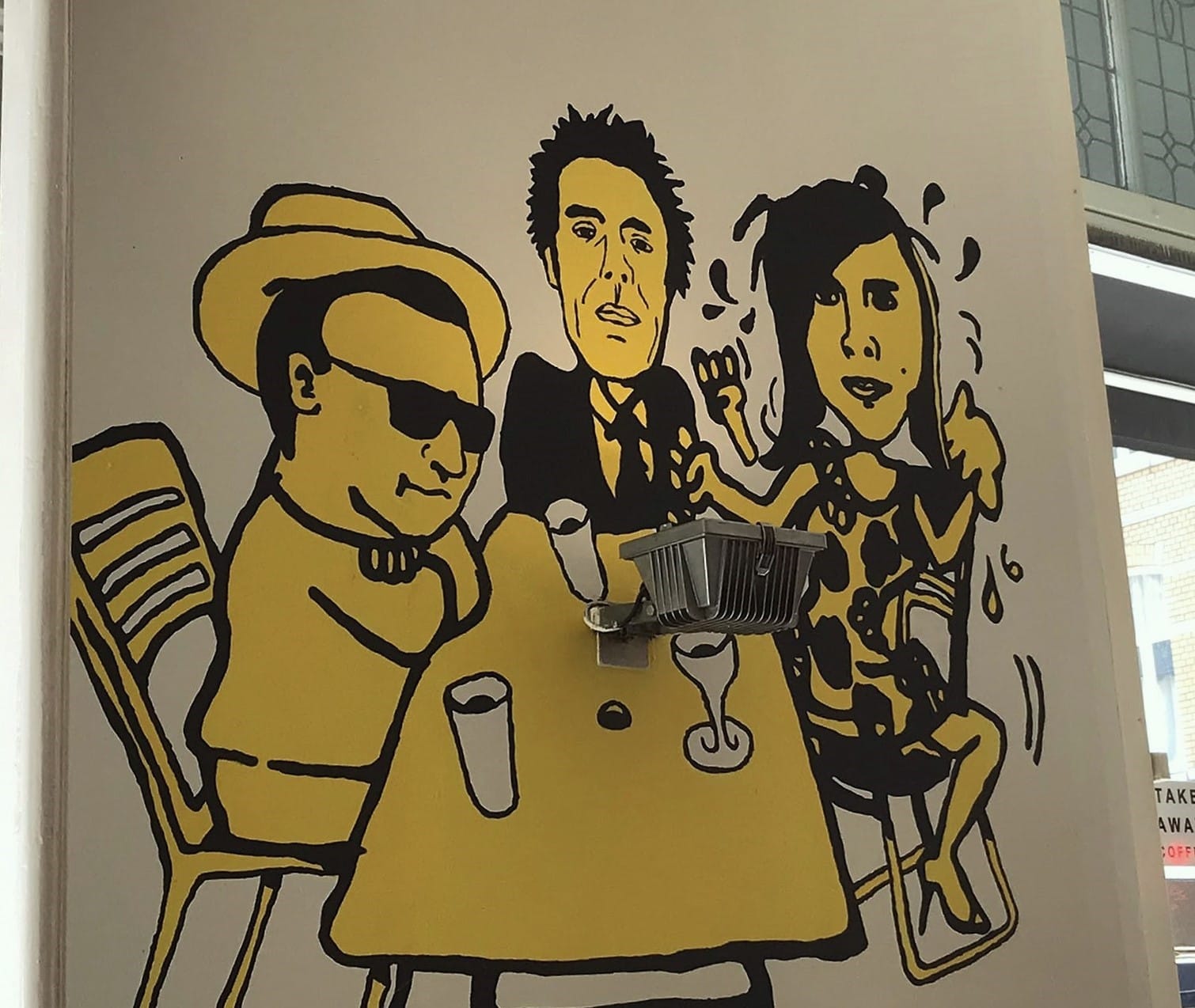 Yellow-and-black mural showing three people gathered around a café table at Café Zondag in Maastricht.