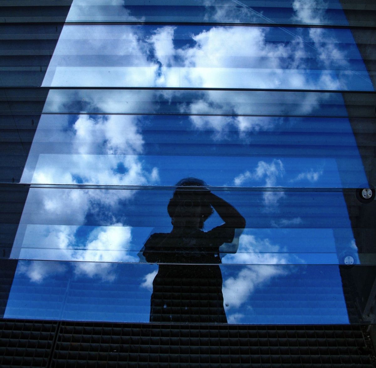 A human silhouette reflected against clouds in the layered glass façade of a building.