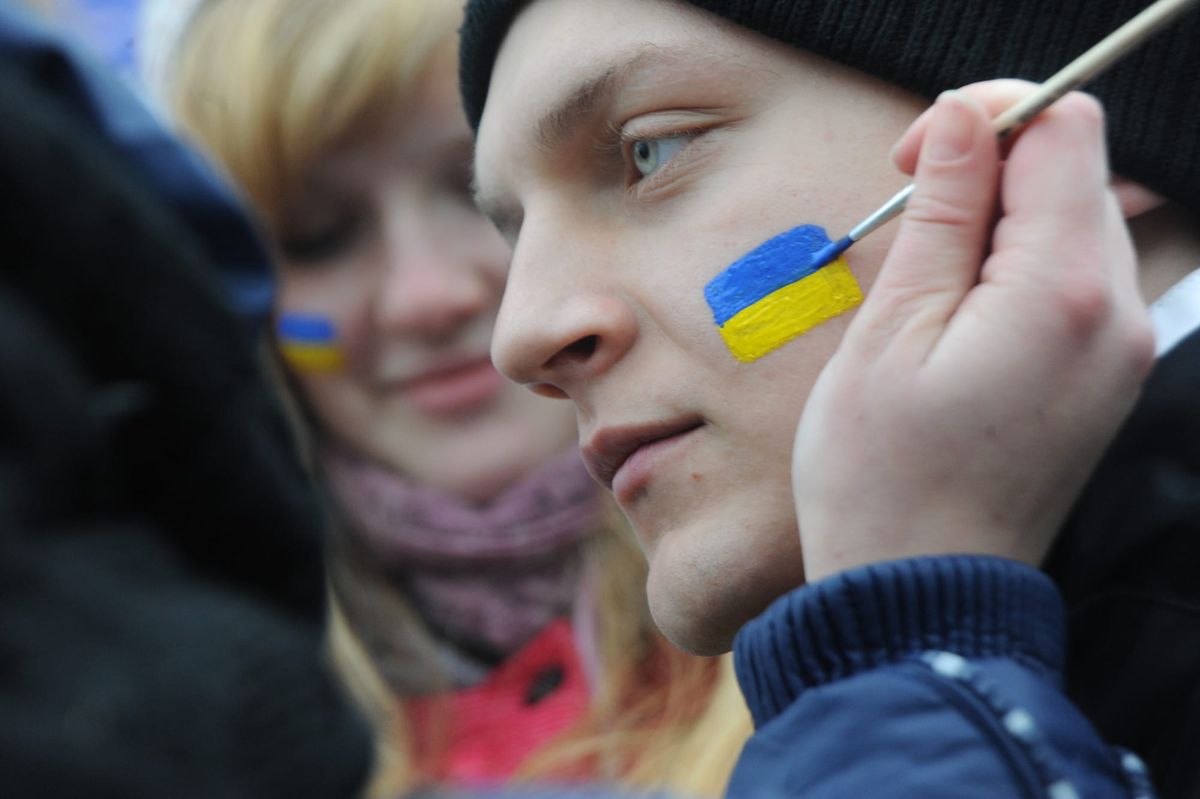 A Ukrainian flag is painted on a protester’s cheek, with another flag-painted face visible behind.