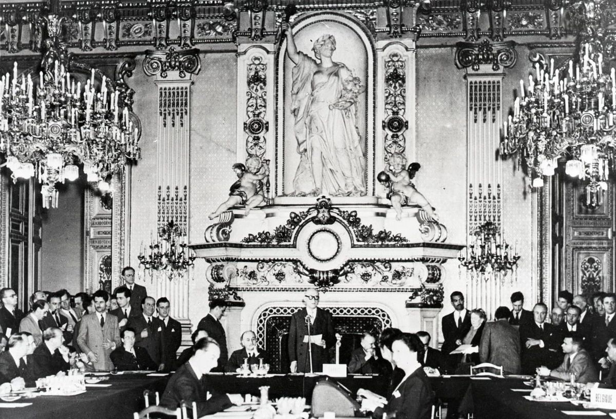 Robert Schuman addresses a gathering in an ornate room, with participants seated around a table.