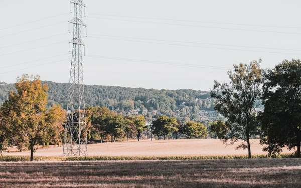 Hoogspanningsmast boven een droog landbouwlandschap met woningen op de achtergrond.