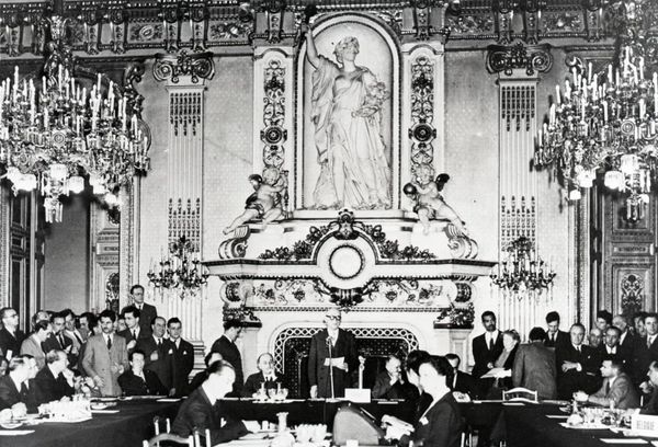 Robert Schuman addresses a gathering in an ornate room, with participants seated around a table.