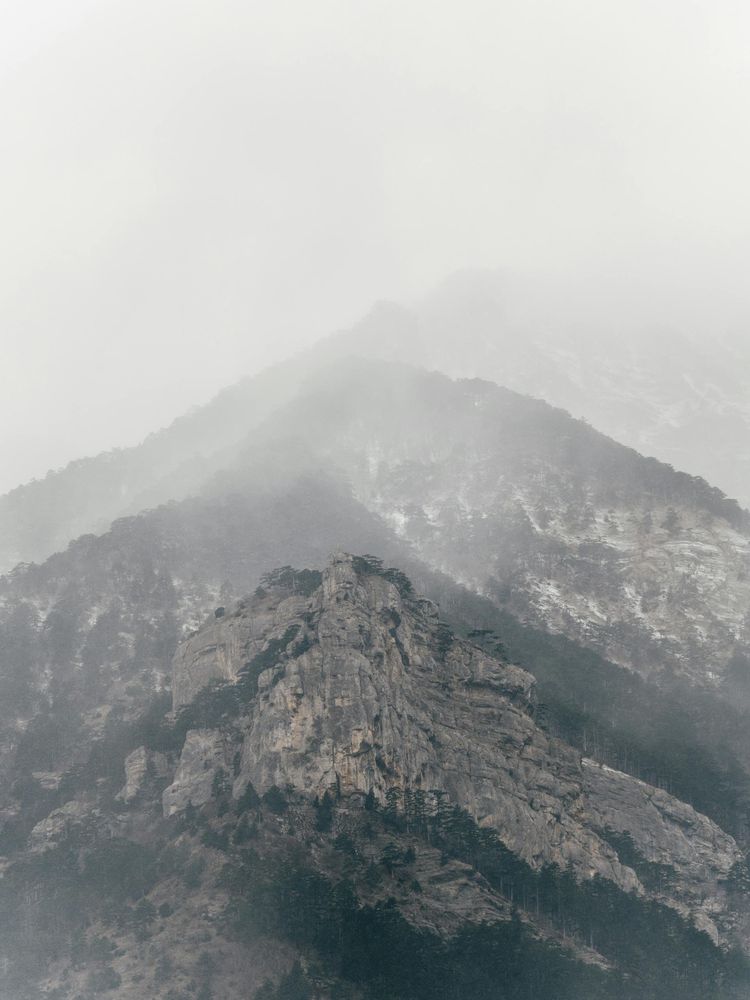 A misty mountain landscape with rocky peaks partly hidden by fog, suggesting truth partly visible through uncertainty.