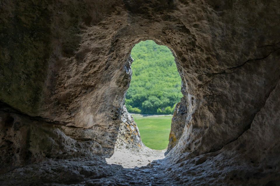 A cave-like rock opening looking out toward a bright green landscape, suggesting the tension between shelter and clearer seeing.