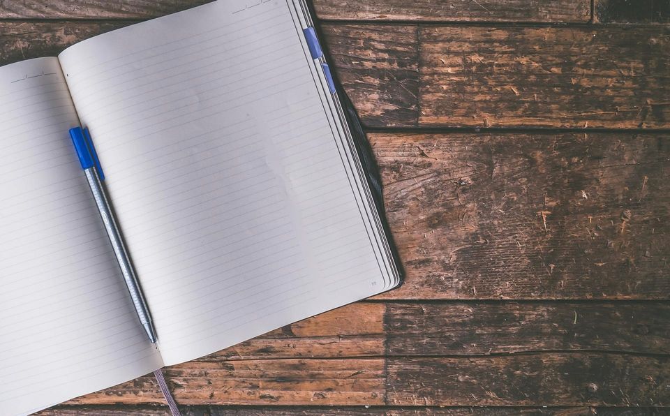 An open notebook and pen on a wooden table, suggesting quiet reflection and self-examination.