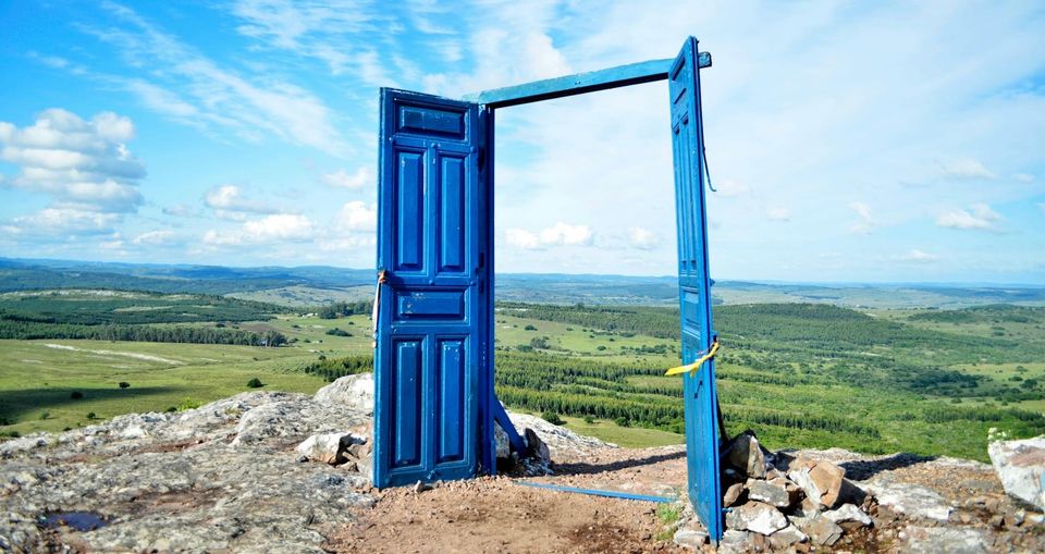 An open blue door standing in a wide landscape, suggesting a beginning or point of entry.