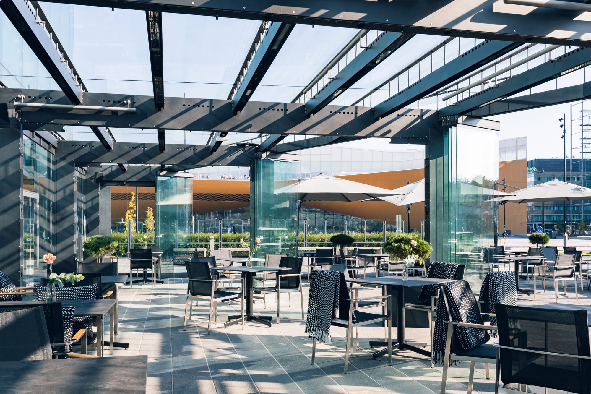 Musiikkitalon osittain katettu terassi, pöytiä ja tuoleja sekä aurinkovarjoja - Venuu.fi