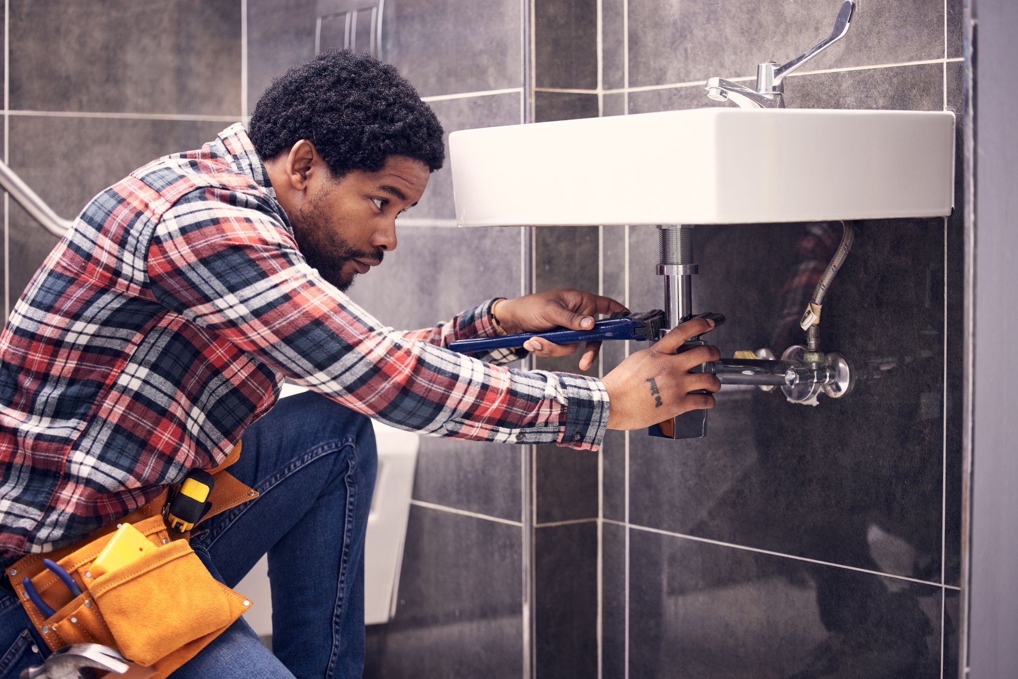 A young man makes repairs under a bathroom sink.