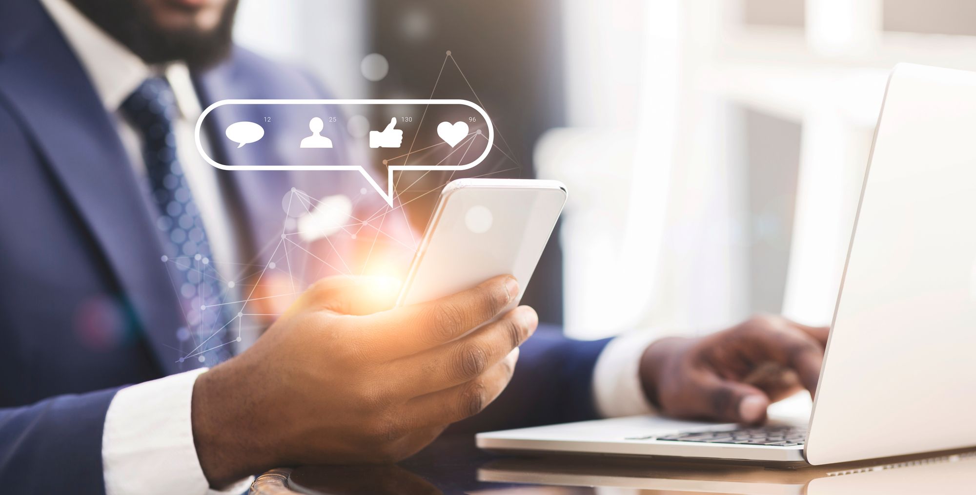 A male real estate agent uses a laptop while also holding their mobile phone and reviewing the engagement in their social media ads.