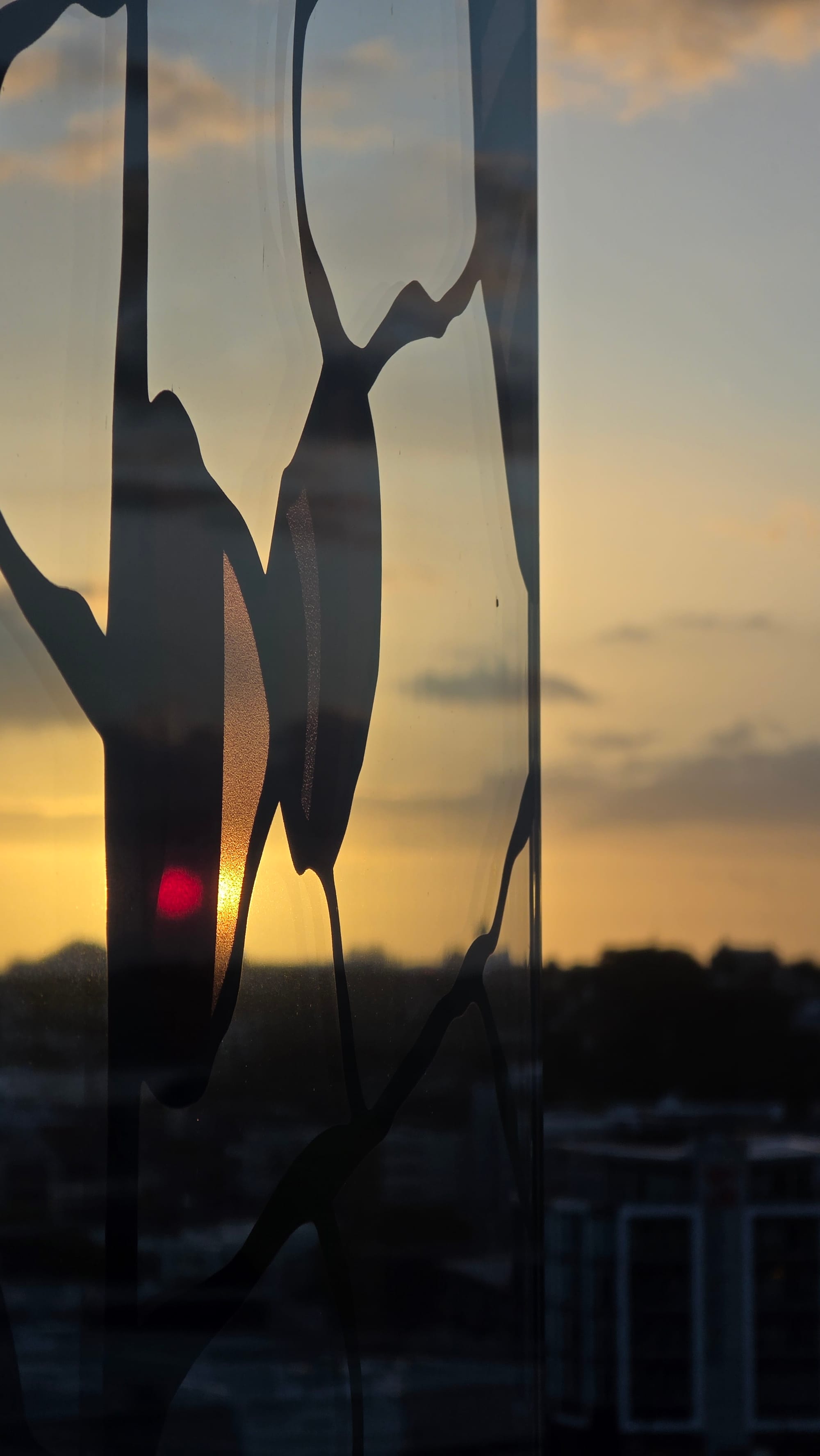 Pattered stained glass tinting an already orange sun red. City skyline out of focus behind.