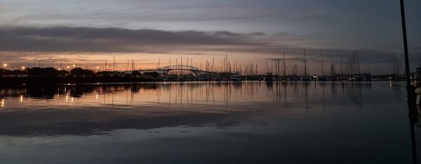 Calm sea reflecting a muted sunset bisected by a line of yacht silhouettes and the Auckland Harbour Bridge 