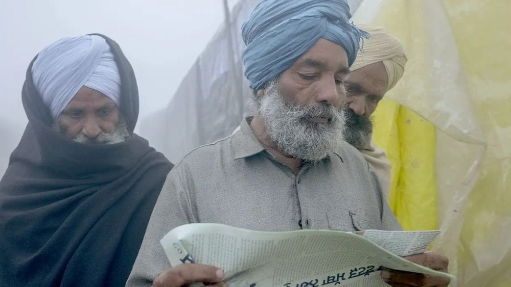 Three Indian men with beards and wearing head wraps read a newspaper.