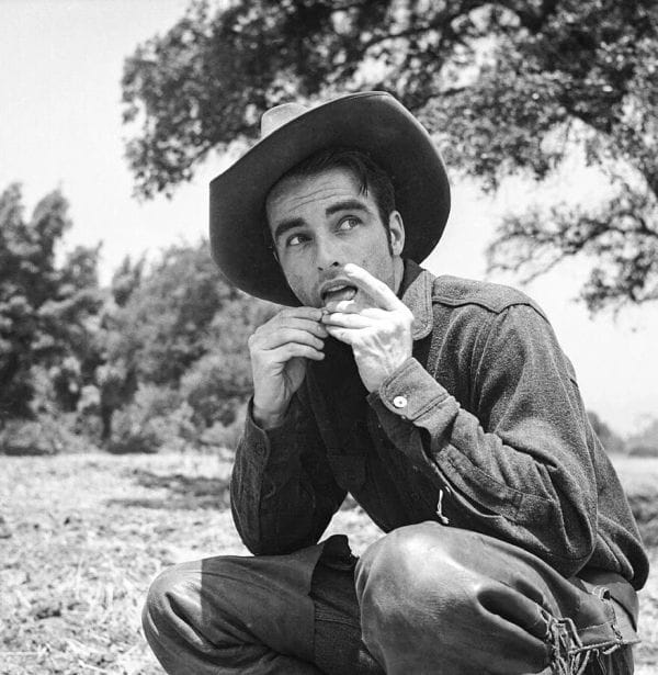Montgomery Clift on set of Red River in a cowboy hat and rolling a cigarette.