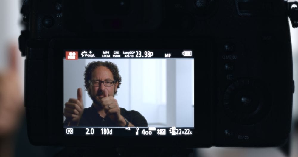 An interview subject holding this thumbs up is seen through the view-screen of a digital camera.