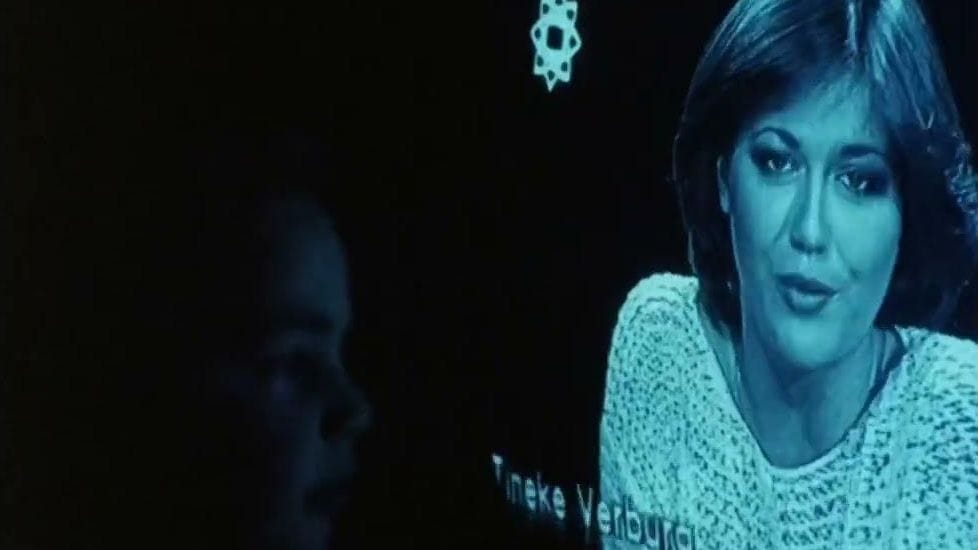A young child looks close-up at a television with a woman's face on it, the image is glowing blue.