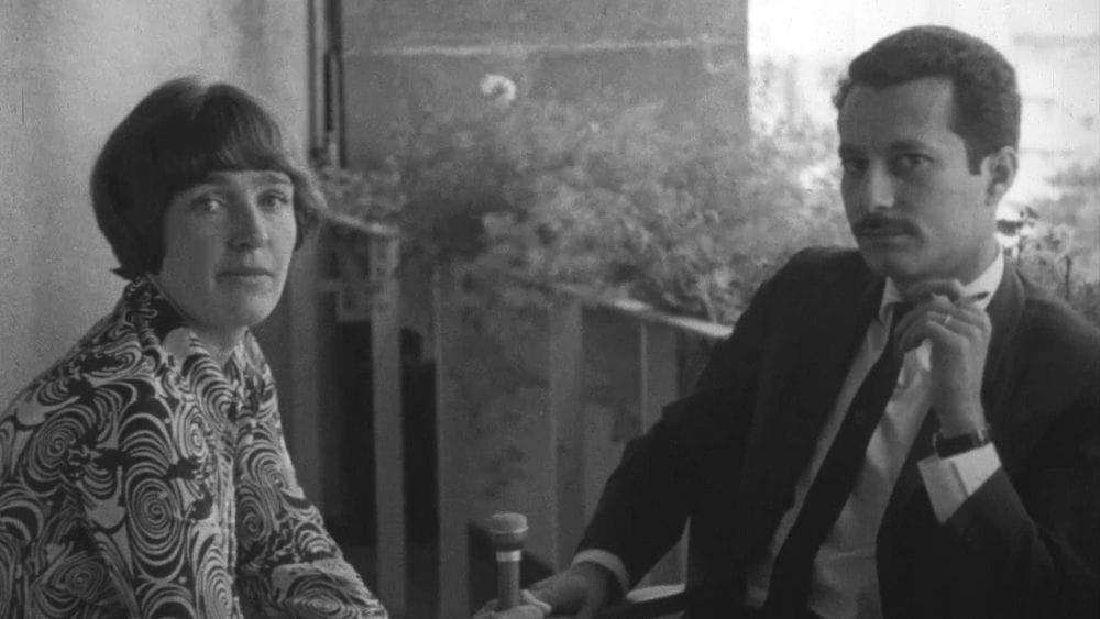 Black and white archive photo of a female swedish journalist interviewing a Palestinian man in a suit smoking a cigarette.