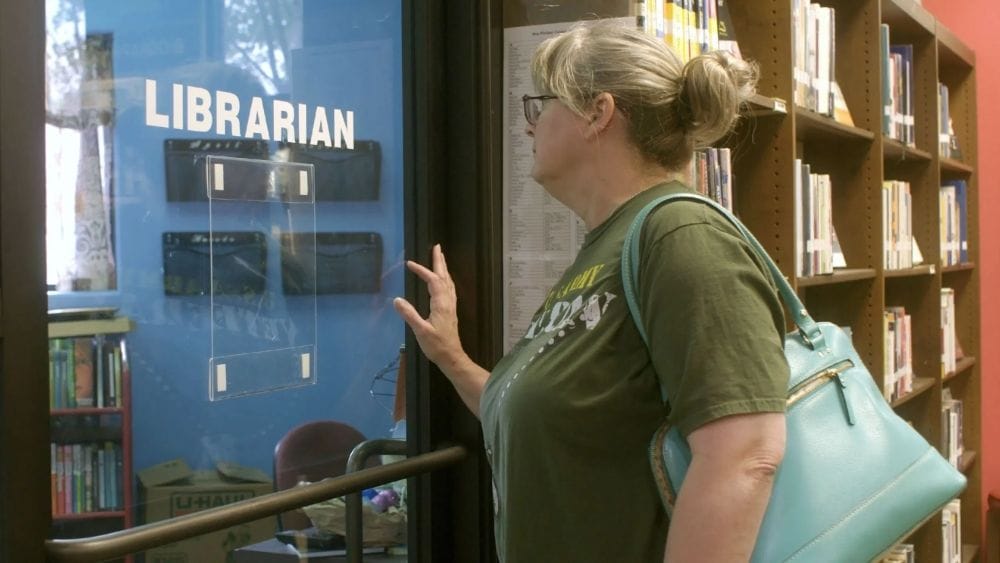A woman looks wistfully through a glass door with the word 'librarian' on it.