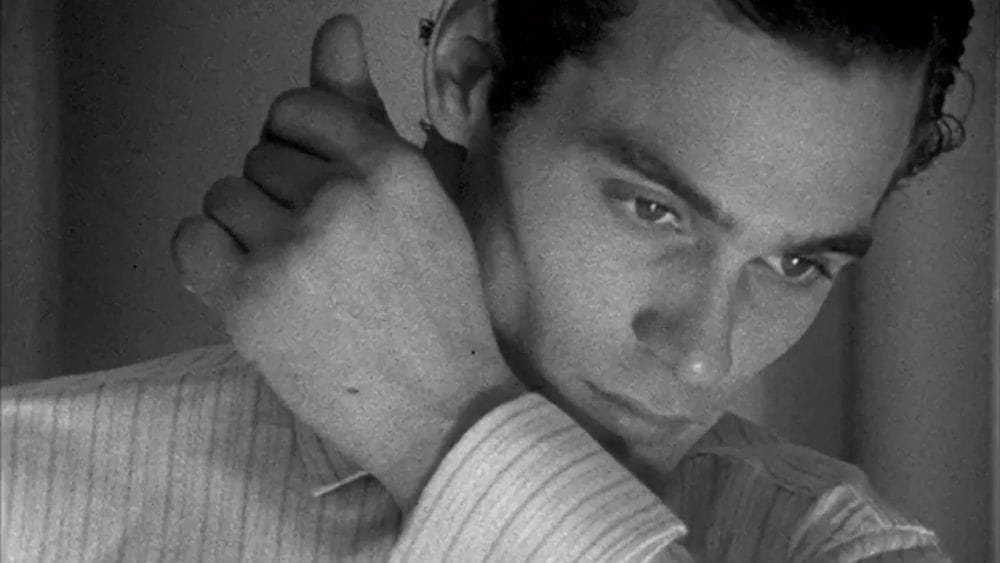 A male model poses with his hand to his face showing off the cuff of a business shirt.