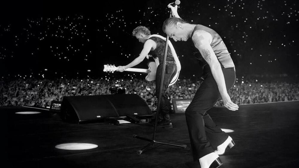Black and white image from the stage of a concert as a longer and guitar player perform in front of thousands of people.