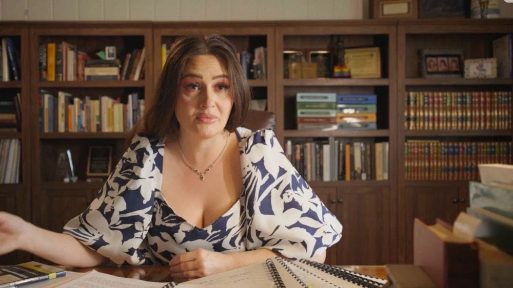 A female lawyer in a blue and white patterned dress sits at her desk that is covered in files and binders.