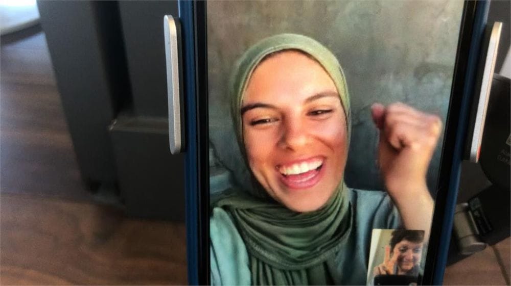A Palestinian woman in head scalf and smiling a large toothy grin appears on the screen of a smart device.
