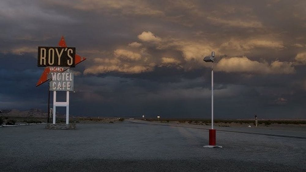 An old motel vacancy sign on a stretch of empty highway underneath clouds.