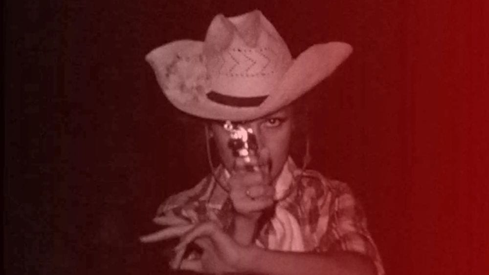 A man in a cowboy hat aims a gun directly in front of him.