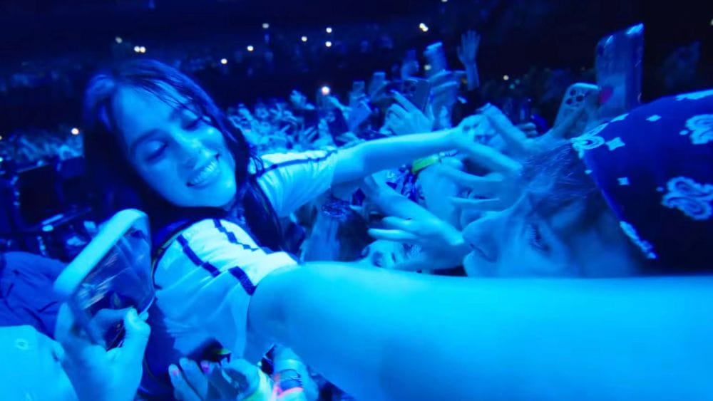 Bathed in blue light, Billie Eilish extends her arms out into the concert crowd.