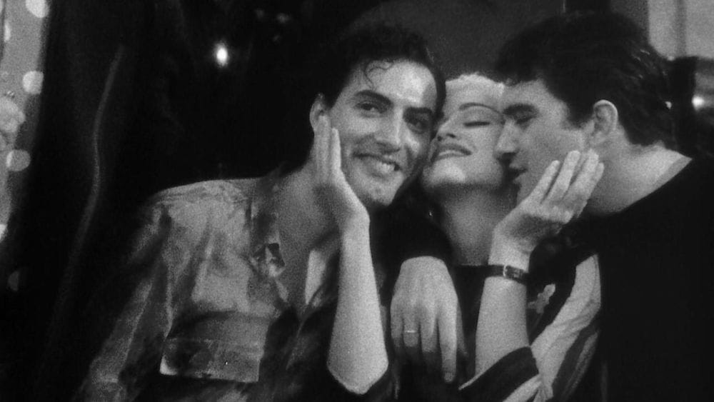 Madonna sits between two men with her hands to their faces, one of them is Antonio Bandares.