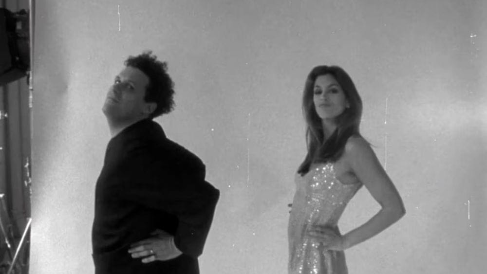 Isaac Mizrahi and a supermodel flaunt in front of a camera in black and white.