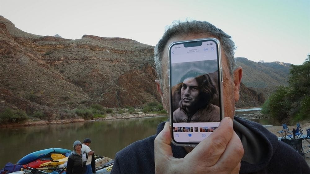 A man holds an iPhone to his face showing his younger self.
