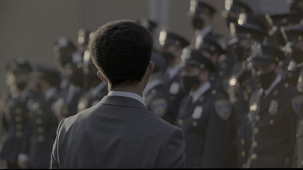 A black mayor in a suit stands in front of a squad of police officers.
