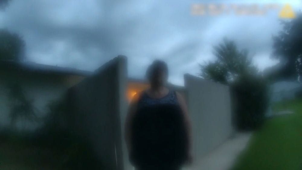 A woman stands outside her home, she and the image around her appear fuzzy due to low quality video that she filmed with.