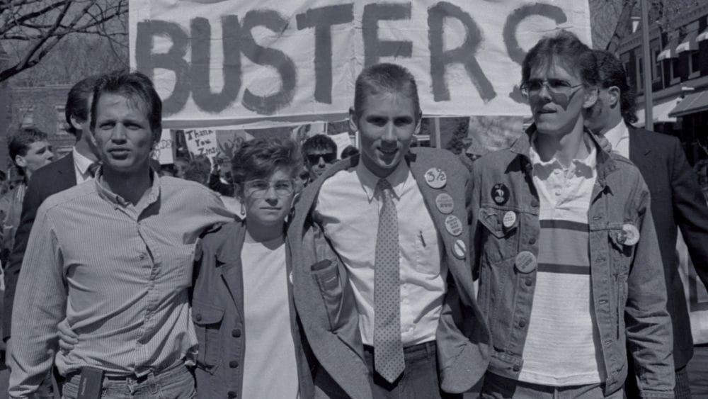 Black and white photo of four young college activists from 1988 arm-in-arm.