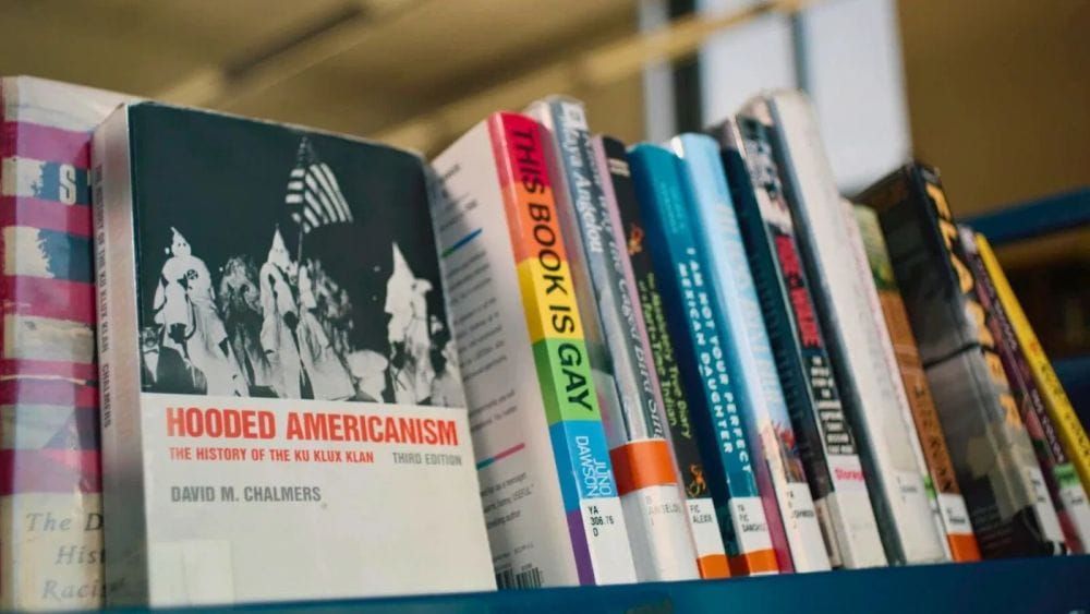 A library bookshelf featuring titles like Hooded Americanism and This Book Is Gay.