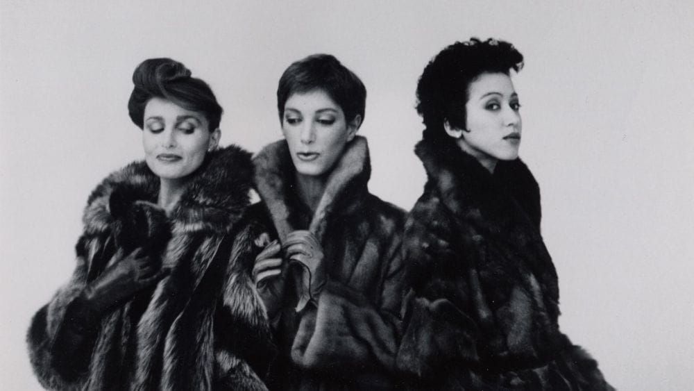 Three dark-haired women pose in fur coats.