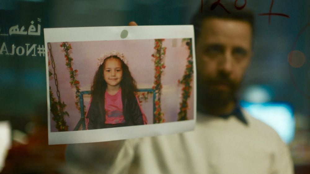 A bearded Palestinian man holds up a photo of a young Palestinian girl dressed in pink with flowers in her long hair.