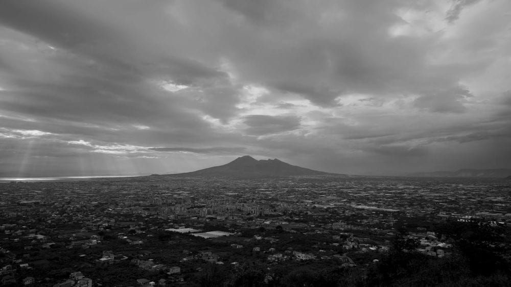 Mount Vesuvius stands tall underneath grey clouds, towering over the city below.