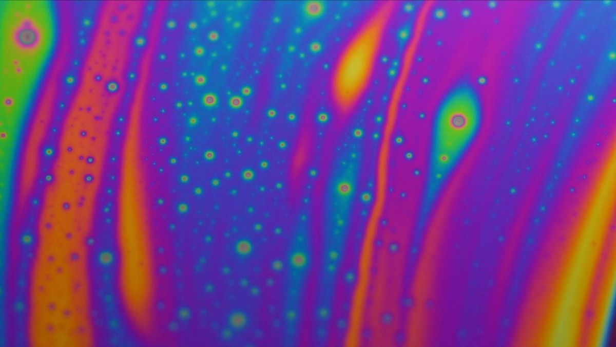 A slick oil effect as purple, orange and green colours clash under a microscope.