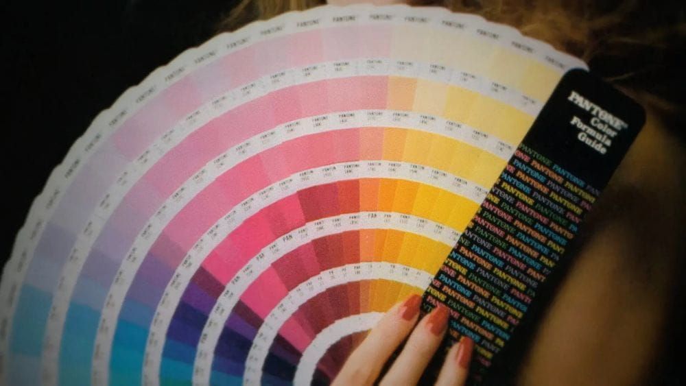 Pantone color swatches fanned out by a hand with long painted-red nails.