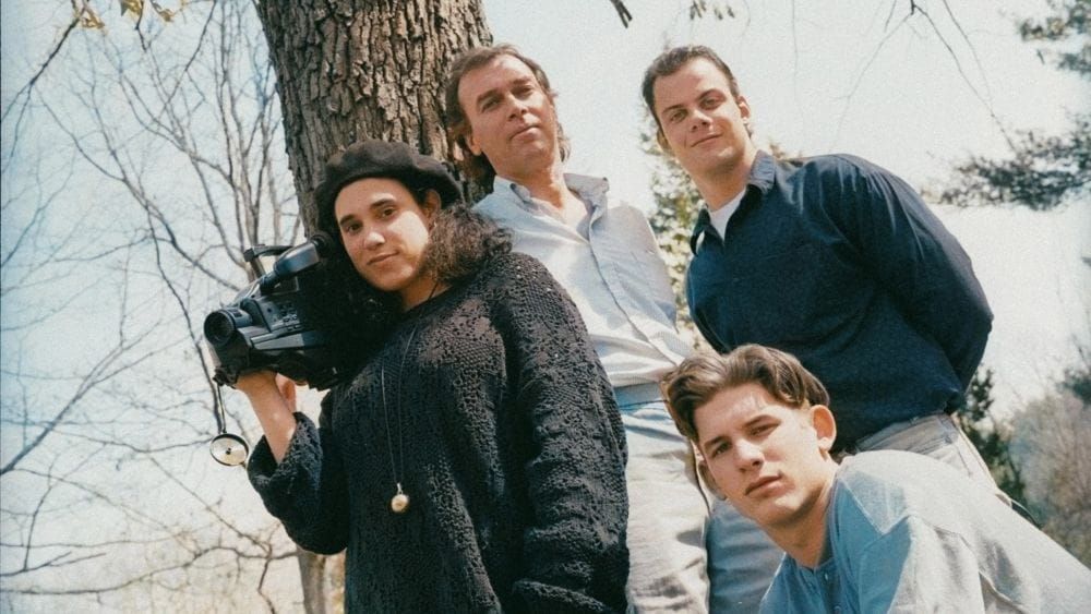 Three high school students in 1991 outdoors with their teacher. One holds a video camera.