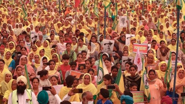 A large protest featuring hundreds of marching men and women, many wearing yellow or orange, with some holding signs or flags.