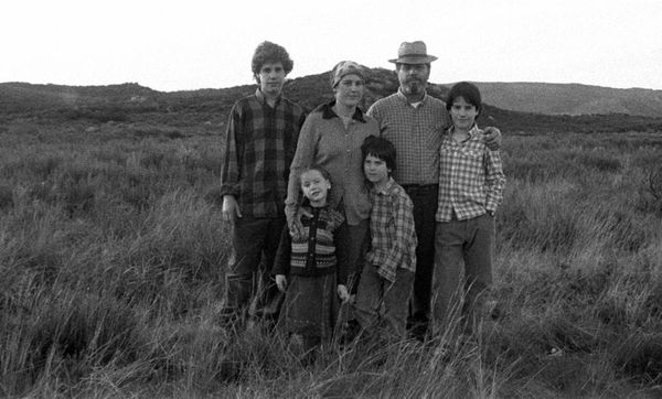 A black and white photography of a mother, father and their four children stand in an empty, grassy field.